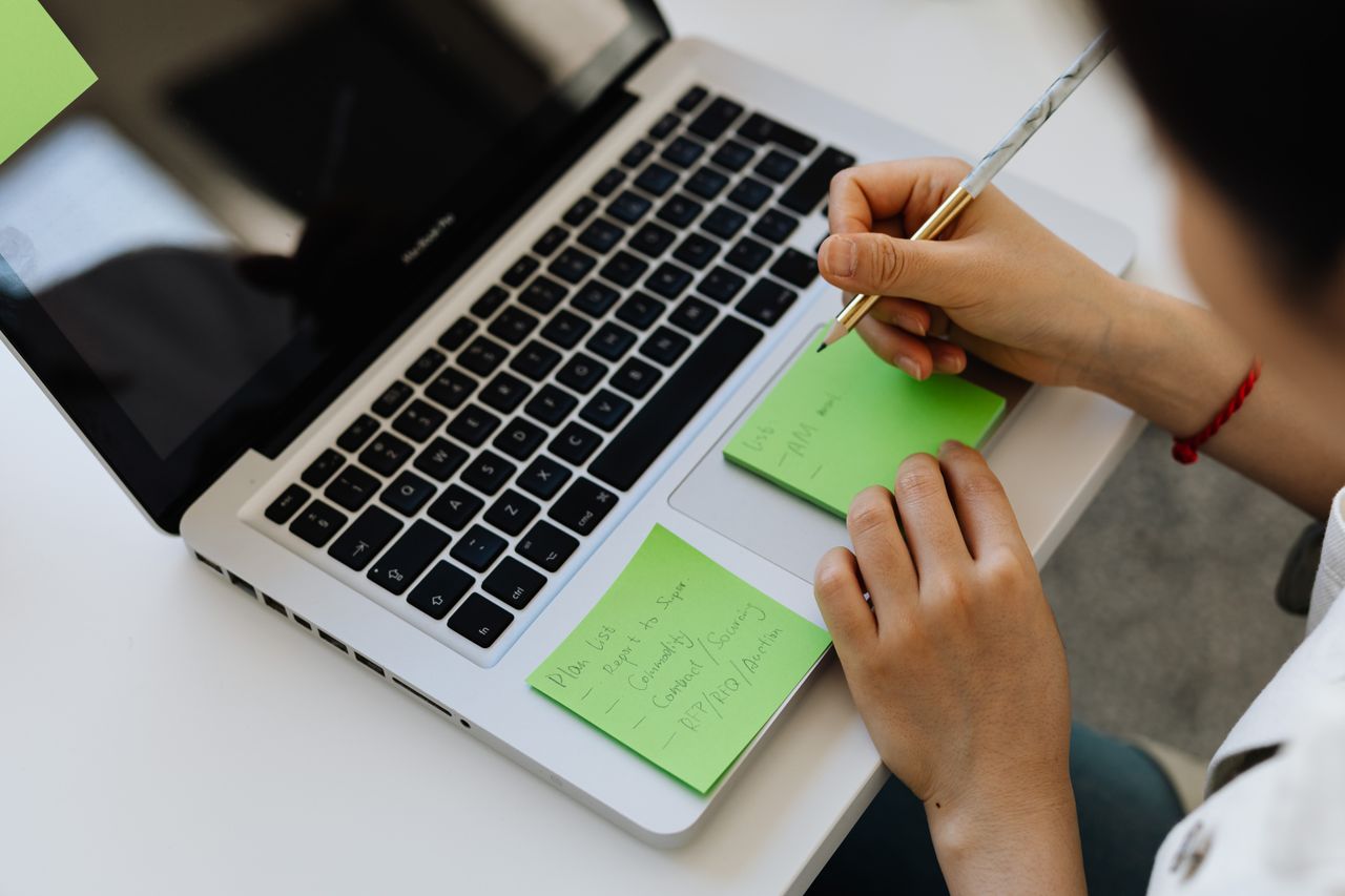 Services An individual writes notes on green sticky notes placed on a laptop in a work setting.
